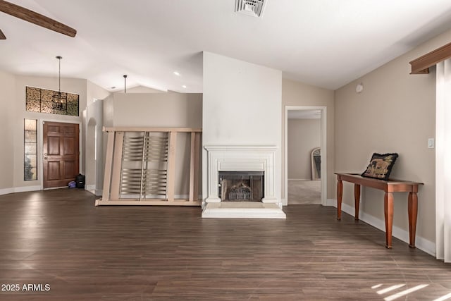 living area with visible vents, lofted ceiling, a fireplace with raised hearth, wood finished floors, and baseboards