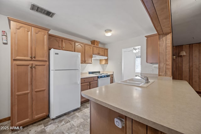 kitchen featuring sink, white appliances, ceiling fan, wooden walls, and kitchen peninsula