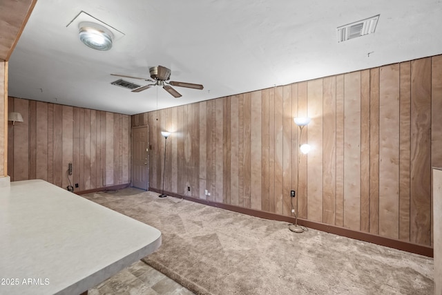 carpeted spare room featuring wooden walls and ceiling fan