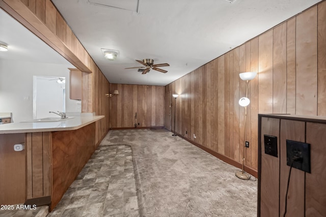 interior space with light carpet, sink, wooden walls, and ceiling fan