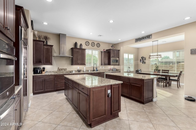 kitchen featuring a wealth of natural light, a kitchen island, hanging light fixtures, and wall chimney exhaust hood