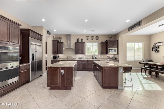 kitchen with sink, built in appliances, wall chimney exhaust hood, a kitchen island, and light stone counters