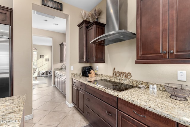 kitchen featuring black electric stovetop, wall chimney range hood, light stone countertops, light tile patterned flooring, and stainless steel built in refrigerator