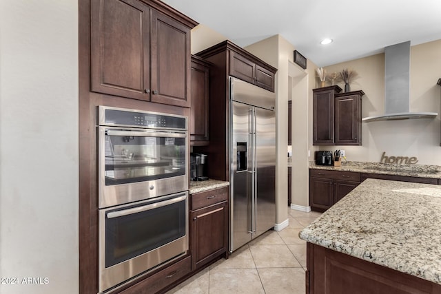 kitchen featuring wall chimney exhaust hood, dark brown cabinetry, light tile patterned floors, and stainless steel appliances