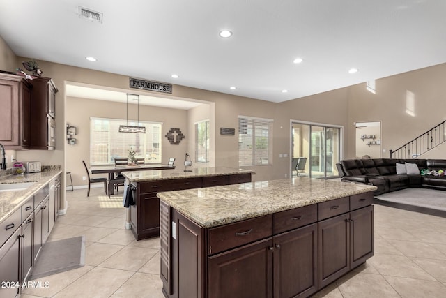 kitchen with light stone countertops, a center island, sink, pendant lighting, and dark brown cabinets