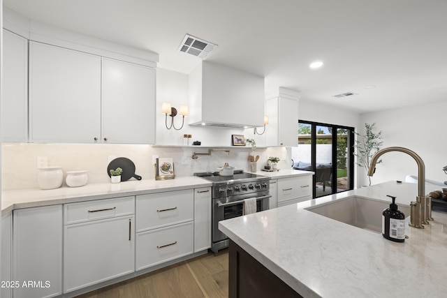 kitchen featuring wall chimney range hood, high end stainless steel range, a sink, and visible vents