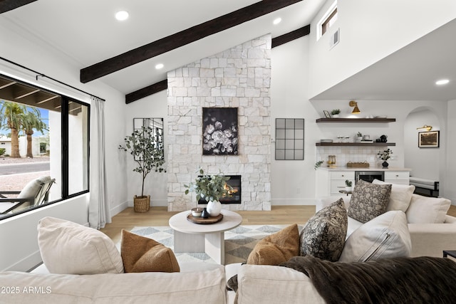 living room with a dry bar, visible vents, light wood-type flooring, a fireplace, and beam ceiling