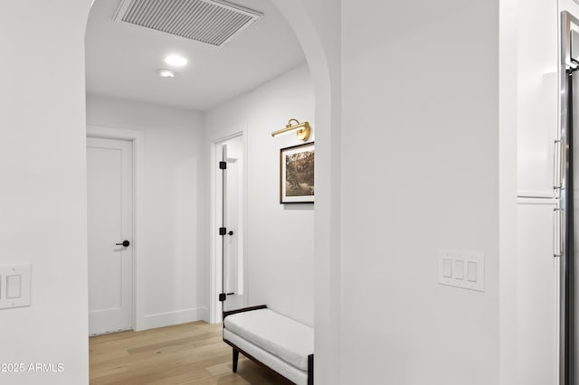 corridor with arched walkways, baseboards, visible vents, and light wood finished floors