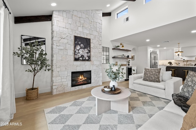 living room featuring light wood finished floors, visible vents, beamed ceiling, a high ceiling, and a fireplace