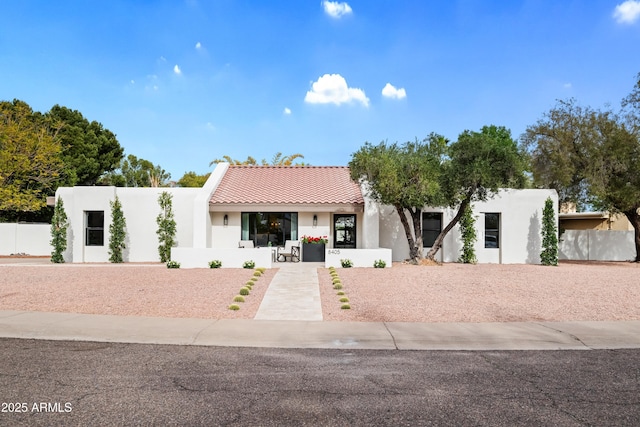 view of front of house with fence, a tile roof, and stucco siding