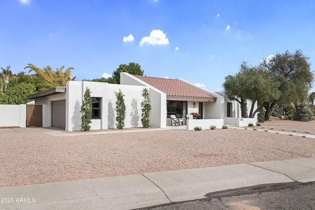 view of front of house featuring a garage, a tile roof, fence, and stucco siding