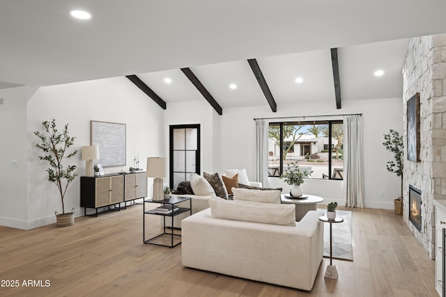 living area featuring vaulted ceiling with beams, light wood-style floors, baseboards, and a stone fireplace