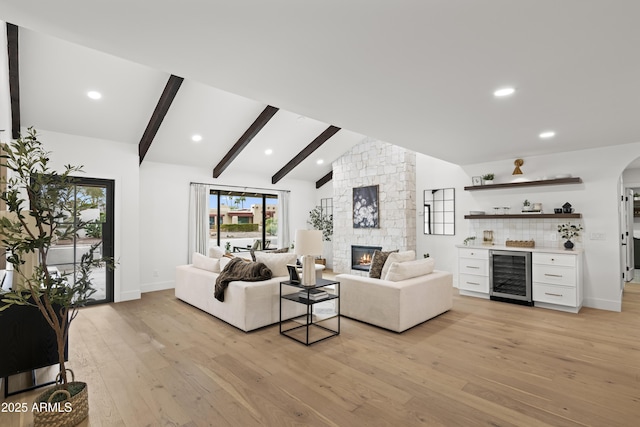 living room featuring lofted ceiling with beams, beverage cooler, light wood-style flooring, and a stone fireplace