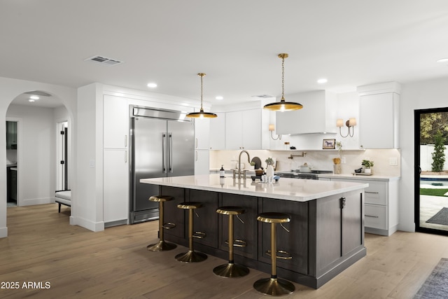 kitchen with visible vents, arched walkways, a sink, stainless steel built in fridge, and backsplash