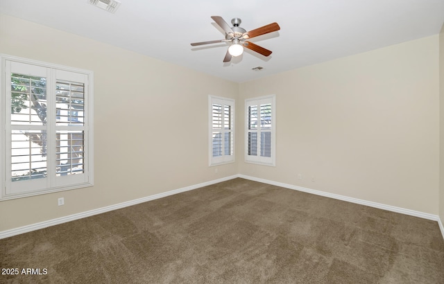 spare room with a ceiling fan, visible vents, dark carpet, and baseboards