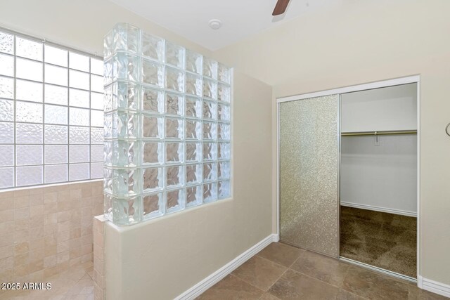 bathroom with baseboards, a spacious closet, a ceiling fan, and a healthy amount of sunlight