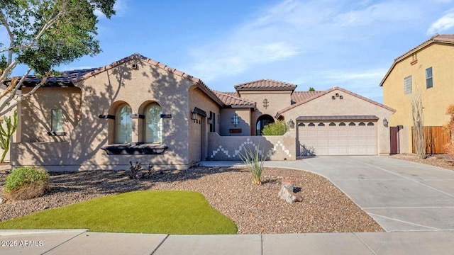 mediterranean / spanish-style home featuring stucco siding, concrete driveway, an attached garage, fence, and a tiled roof