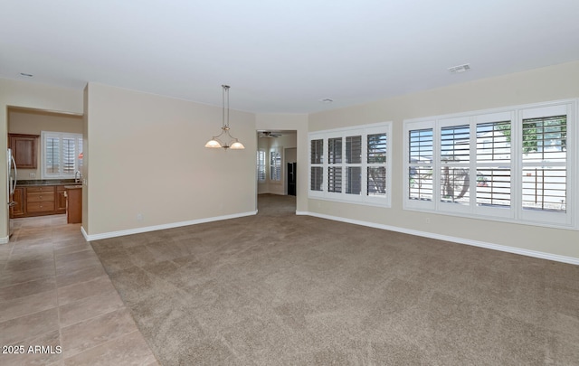 spare room with light tile patterned floors, visible vents, a ceiling fan, light carpet, and baseboards