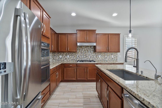 kitchen with light stone countertops, appliances with stainless steel finishes, decorative light fixtures, sink, and backsplash