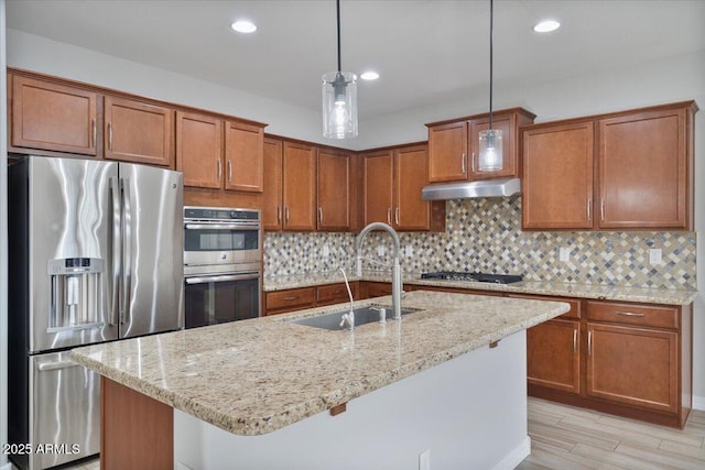 kitchen with stainless steel appliances, a kitchen island with sink, decorative light fixtures, light stone countertops, and sink