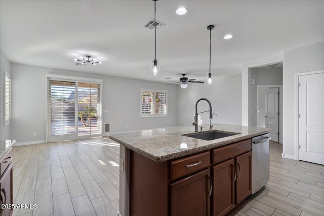 kitchen with ceiling fan, dishwasher, a center island with sink, sink, and light stone countertops