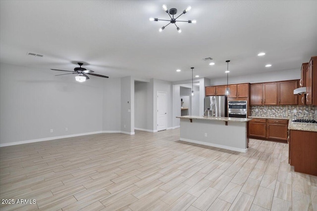 kitchen with light stone countertops, stainless steel appliances, backsplash, hanging light fixtures, and a center island with sink