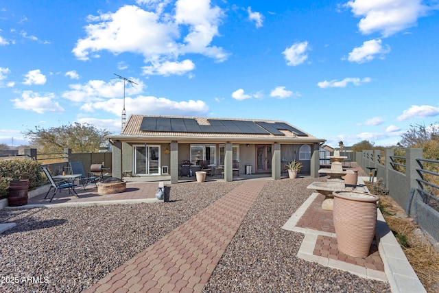 rear view of property with solar panels, a patio area, and an outdoor fire pit