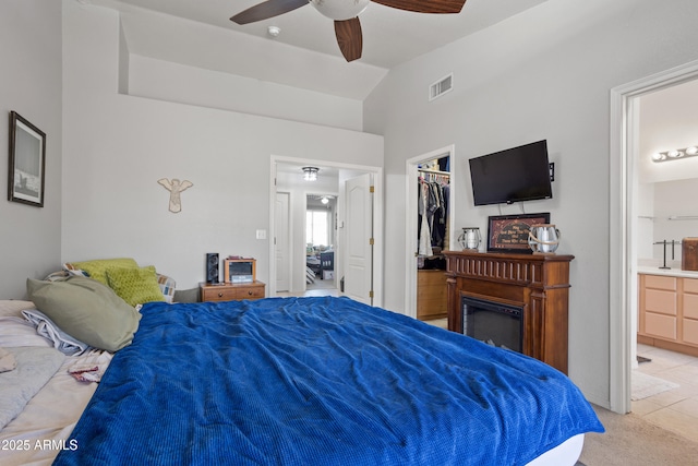 tiled bedroom featuring connected bathroom, a spacious closet, vaulted ceiling, a closet, and ceiling fan