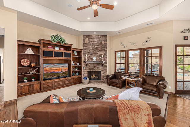 living room with ceiling fan, light hardwood / wood-style floors, a raised ceiling, and a stone fireplace