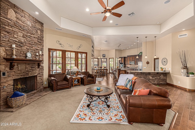 carpeted living room with ceiling fan, a tray ceiling, and a stone fireplace