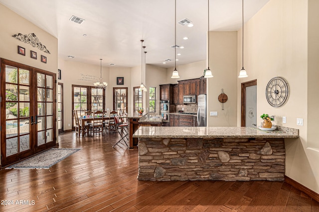 kitchen with a notable chandelier, appliances with stainless steel finishes, dark wood-type flooring, and light stone countertops