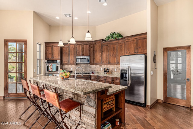 kitchen with stainless steel appliances, decorative light fixtures, dark hardwood / wood-style flooring, and a towering ceiling