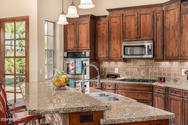 kitchen featuring appliances with stainless steel finishes, backsplash, sink, a center island with sink, and a kitchen breakfast bar