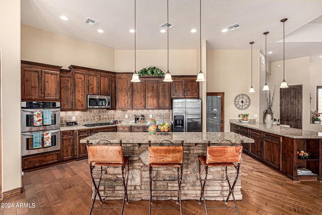 kitchen featuring stainless steel appliances, decorative backsplash, a kitchen bar, an island with sink, and wood-type flooring