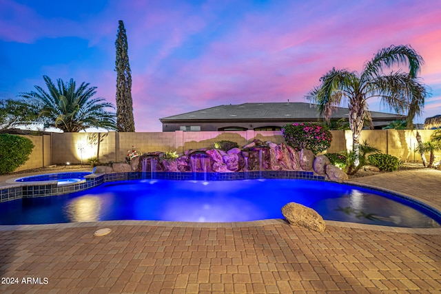 pool at dusk featuring an in ground hot tub, pool water feature, and a patio area