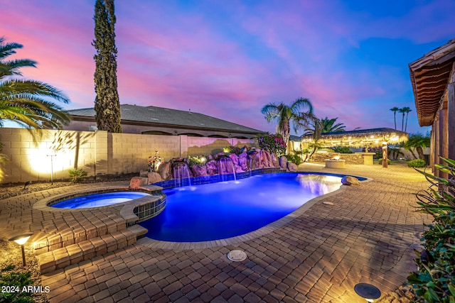 pool at dusk with pool water feature, an in ground hot tub, and a patio area