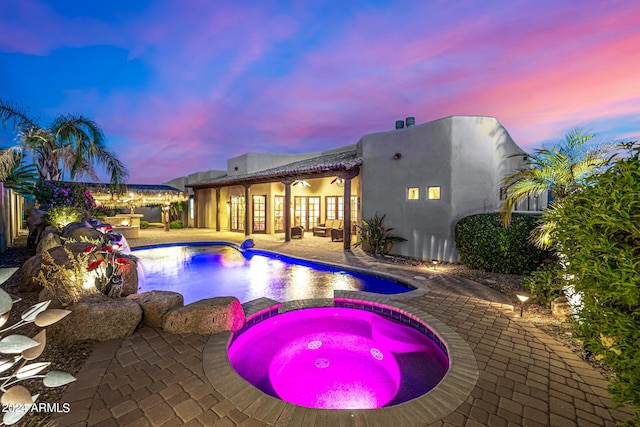 pool at dusk featuring an in ground hot tub and a patio