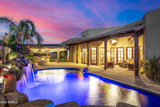 pool at dusk featuring outdoor lounge area, pool water feature, and a patio area