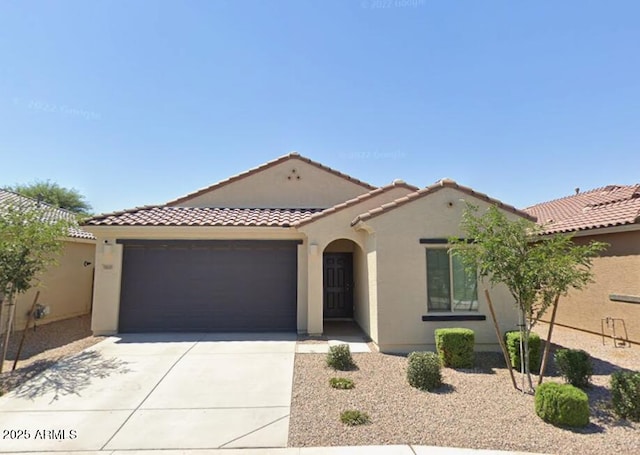 mediterranean / spanish home featuring an attached garage, a tiled roof, driveway, and stucco siding