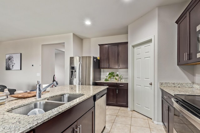 kitchen featuring light tile patterned floors, a sink, dark brown cabinetry, light stone countertops, and stainless steel appliances