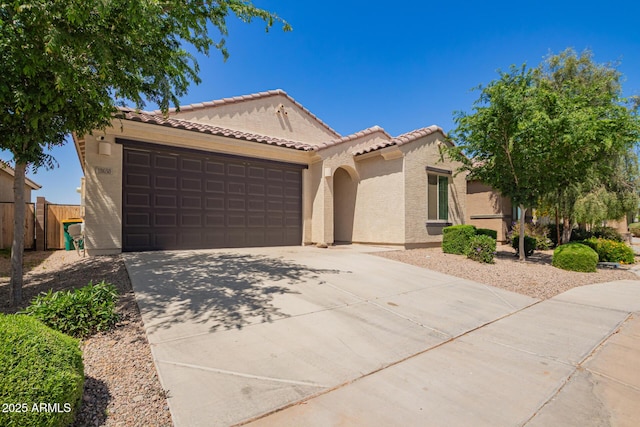 mediterranean / spanish home with a garage, a tile roof, fence, stucco siding, and driveway