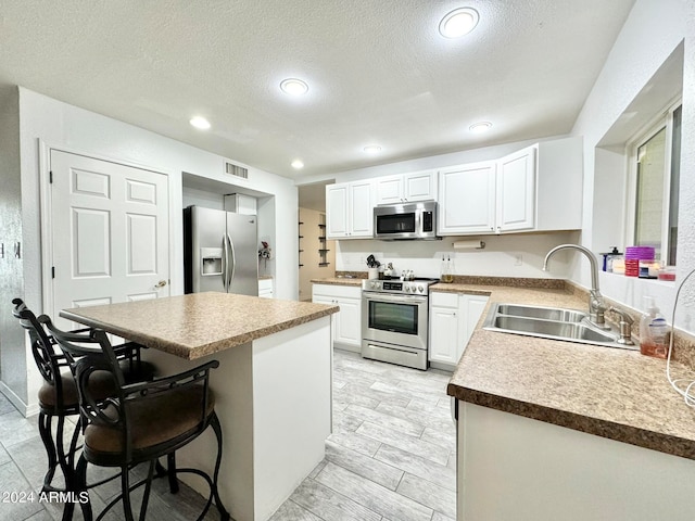 kitchen featuring a textured ceiling, sink, white cabinets, a kitchen breakfast bar, and stainless steel appliances