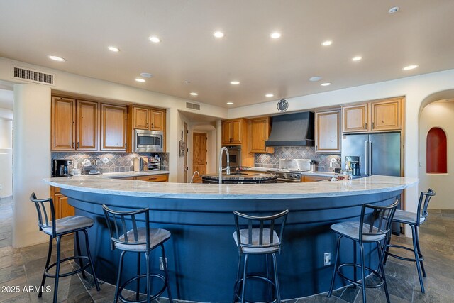 8606 E Arroyo Seco Rd, Scottsdale, AZ 85266 - kitchen featuring stainless steel appliances, wall chimney range hood, tasteful backsplash, recessed lighting, and brown cabinets