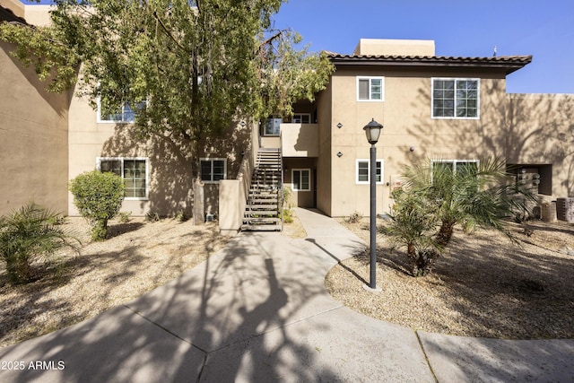 view of front of property with central AC unit, stairway, and stucco siding