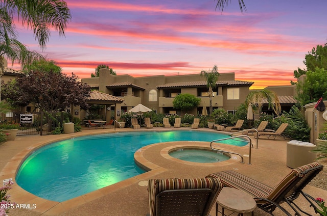 pool at dusk with a community pool, fence, a community hot tub, and a patio