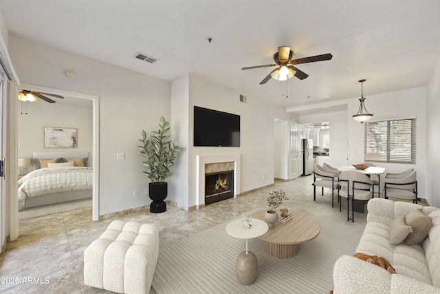 living area with a warm lit fireplace, visible vents, and ceiling fan