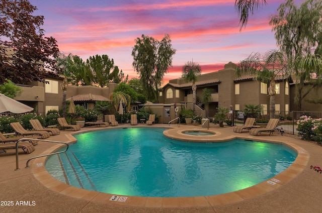 pool at dusk featuring a hot tub, a community pool, fence, and a patio