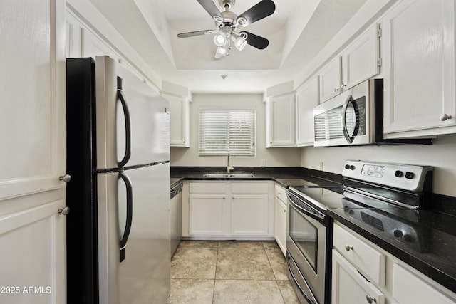 kitchen featuring light tile patterned floors, stainless steel appliances, a sink, white cabinets, and a tray ceiling