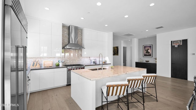 kitchen with an island with sink, premium appliances, light hardwood / wood-style flooring, sink, and wall chimney range hood