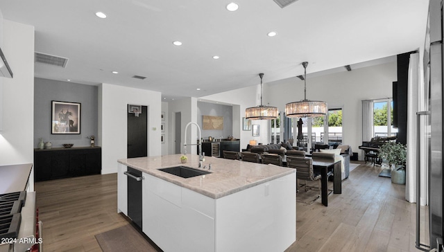 kitchen with light hardwood / wood-style floors, sink, white cabinetry, hanging light fixtures, and a center island with sink